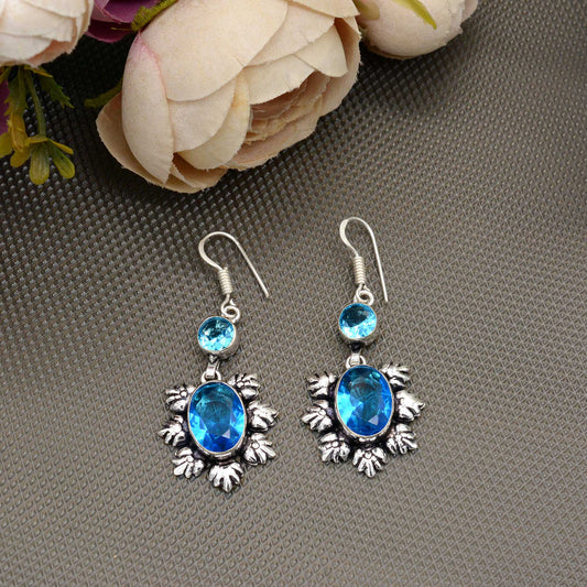 Silver earrings with blue gemstones on a gray surface with flowers in the background