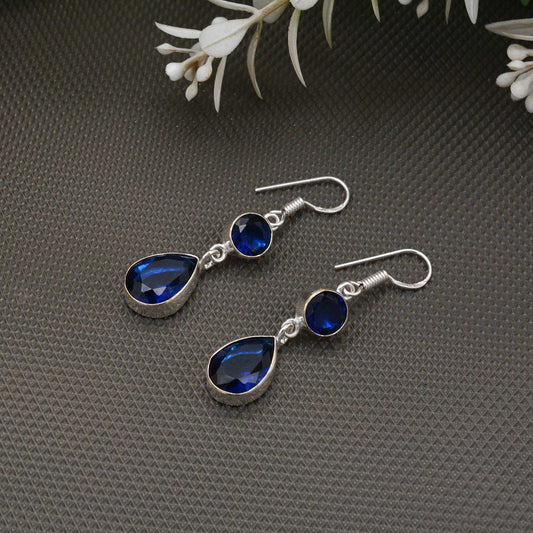 Silver teardrop earrings with blue gemstones on a gray textured surface.