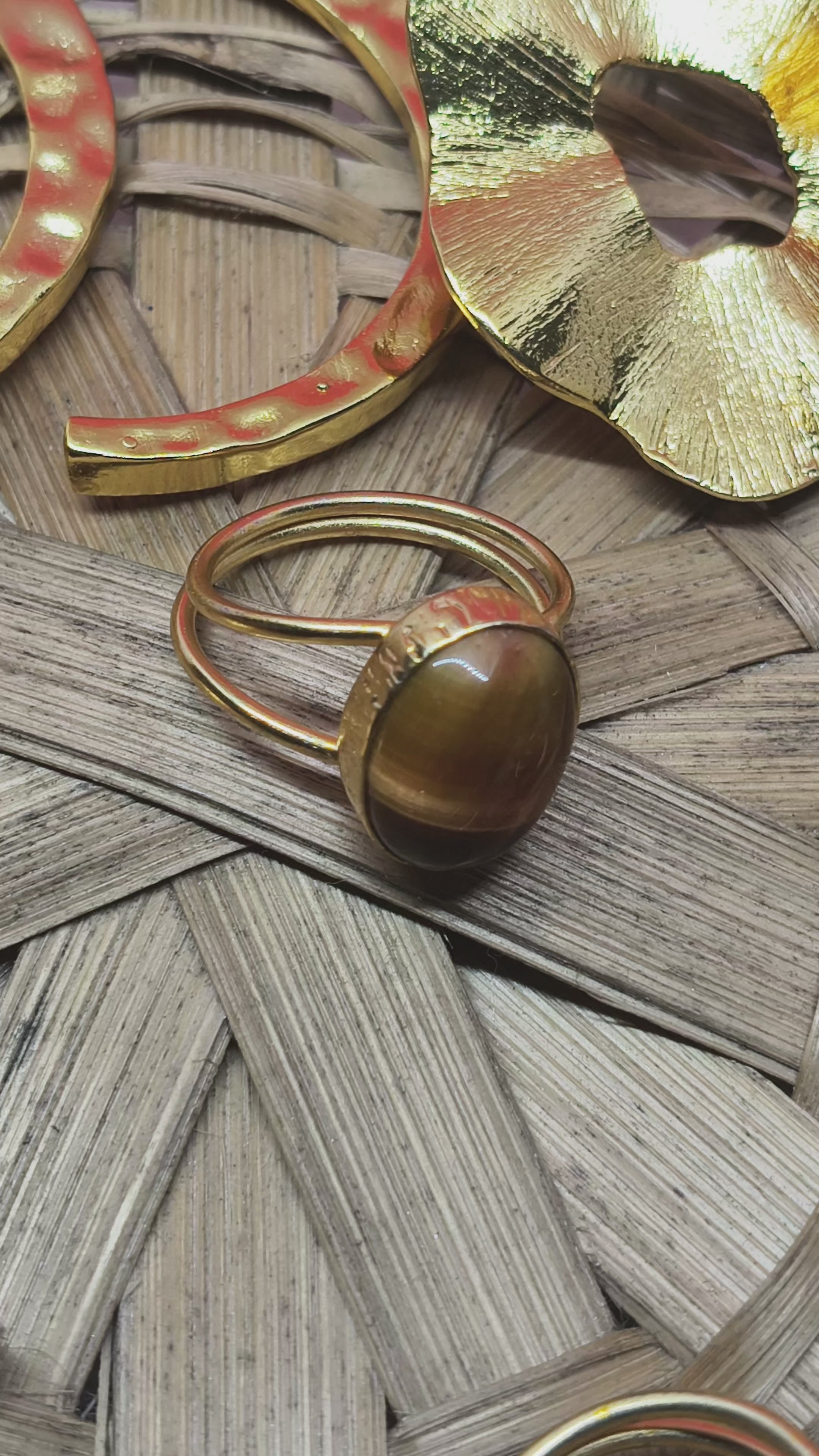 Load video: Flatlay of Relicroot handcrafted 18K gold-plated jewellery including gemstone rings, textured earrings, and artistic statement pieces displayed on a woven round mat.